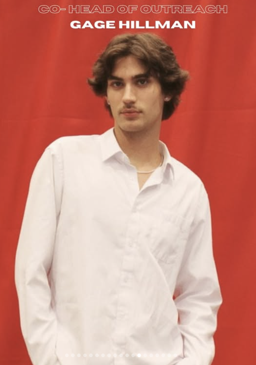 A young man with dark, wavy hair, wearing a white shirt, standing against a red background with text that reads 'CO-HEAD OF OUTREACH GAGE HILLMAN'.