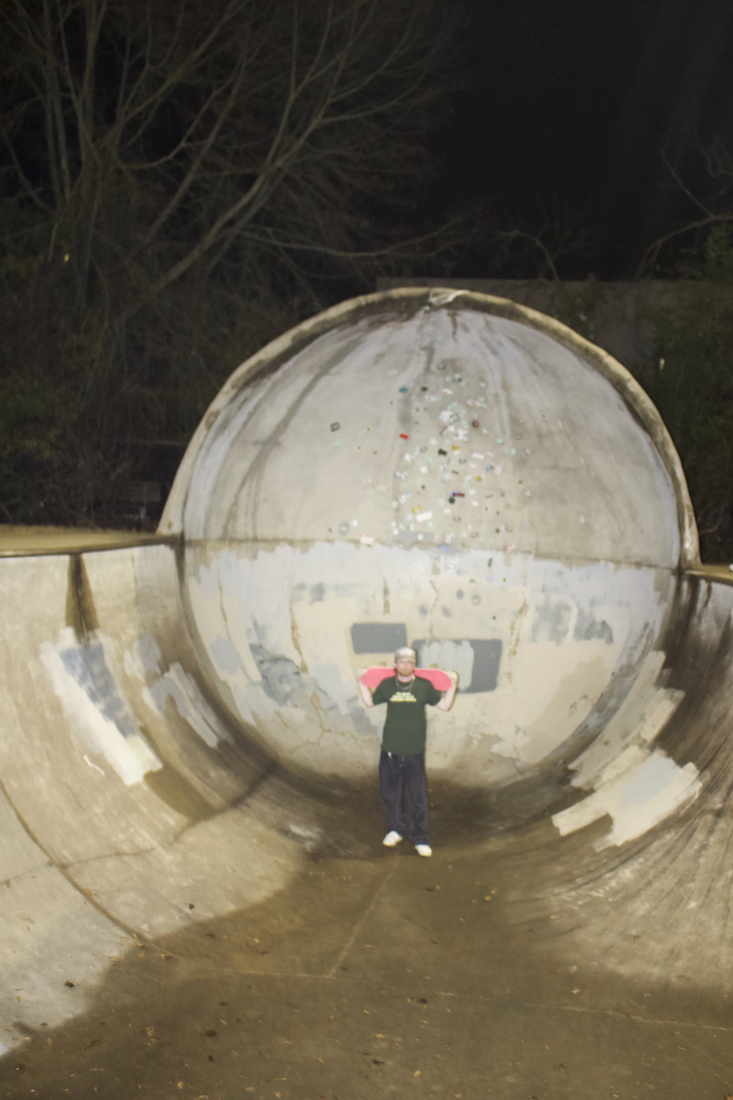 Person taking a selfie in a large, rusted metal pipe at night, with trees visible in the background.