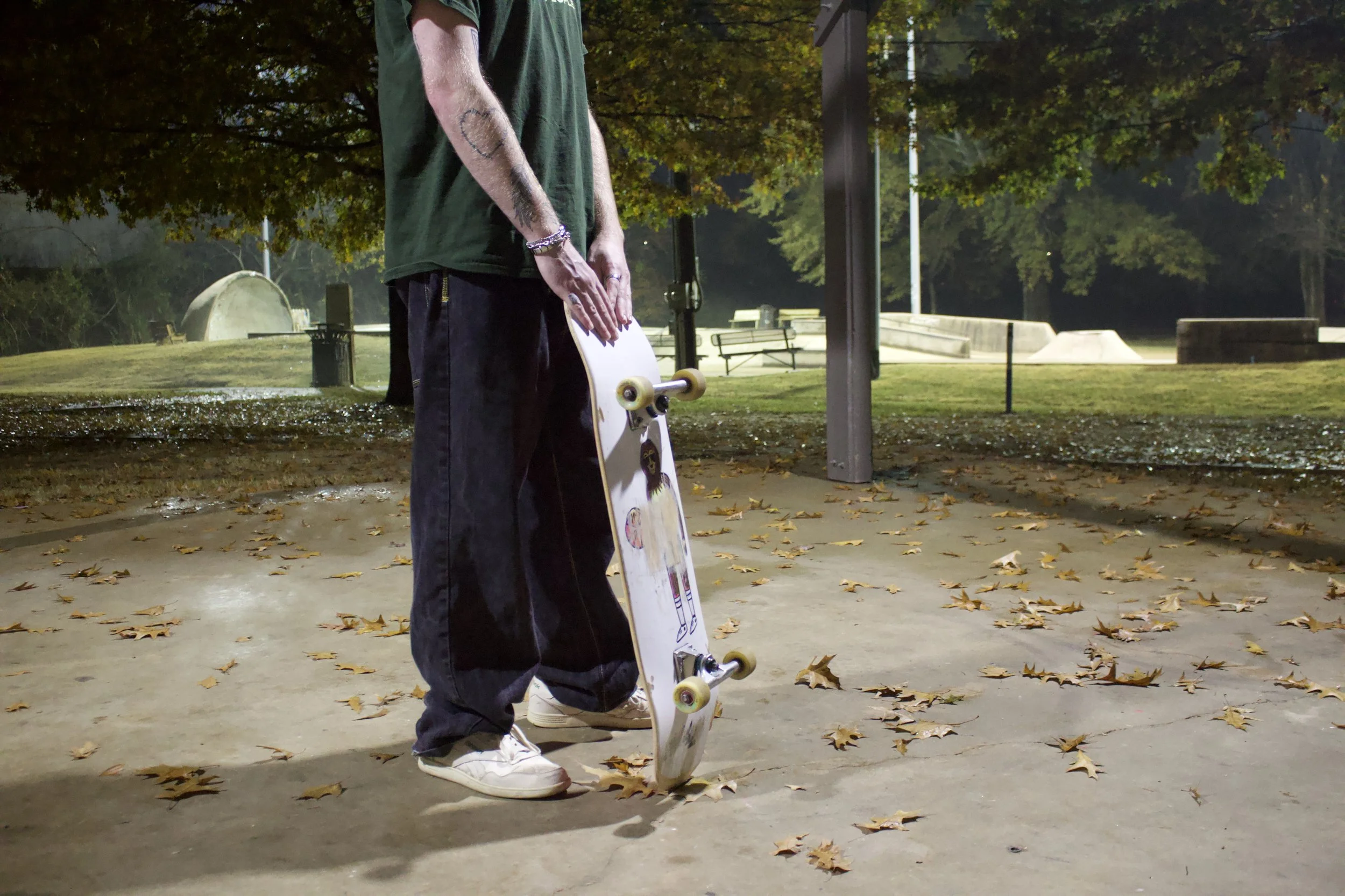 Person standing with a skateboard in a park during fall.