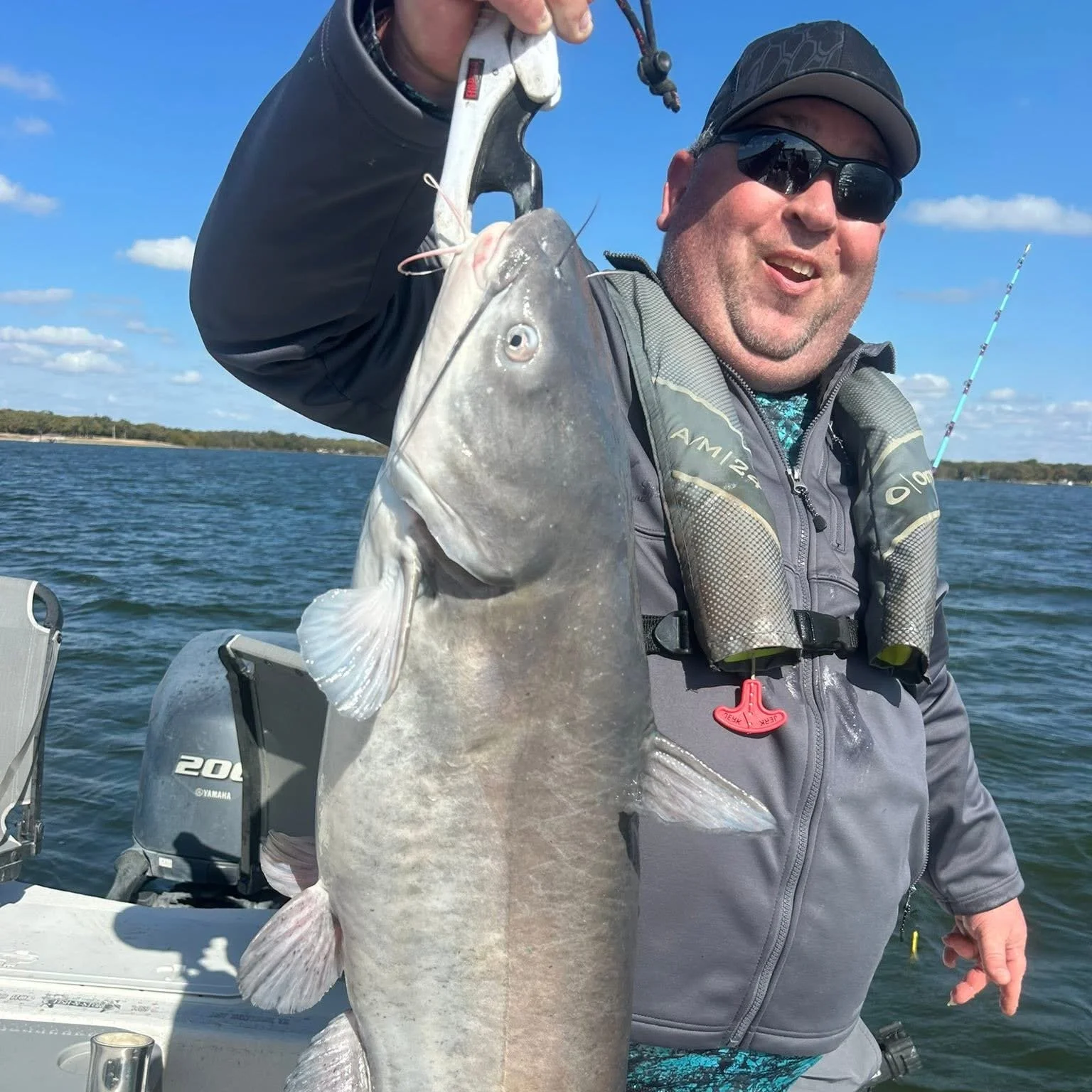 Man holding a large fish on a boat with water and sky in the background.