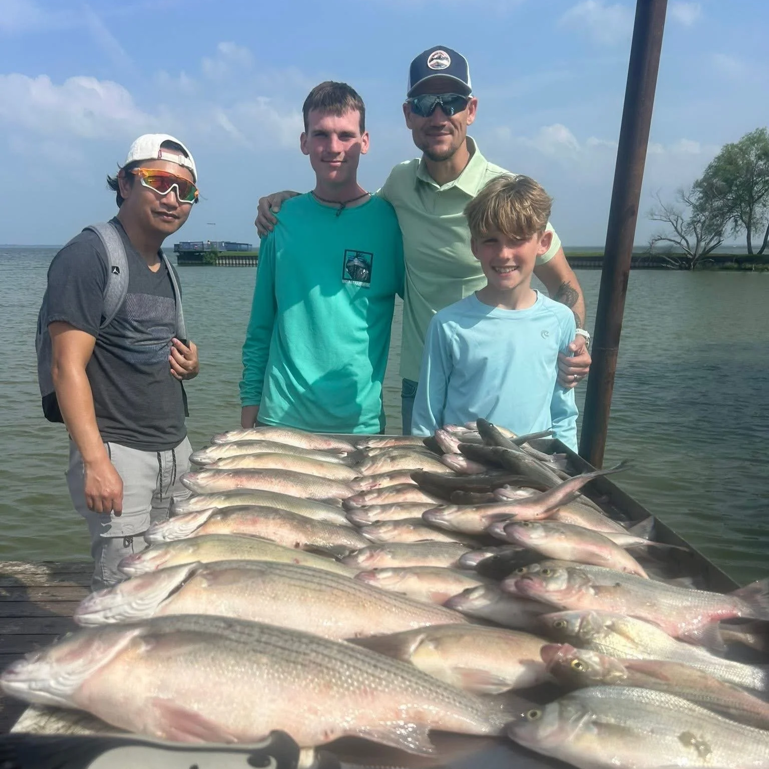 A group of five people, including two children, standing behind a large display of fish in a body of water on a sunny day.