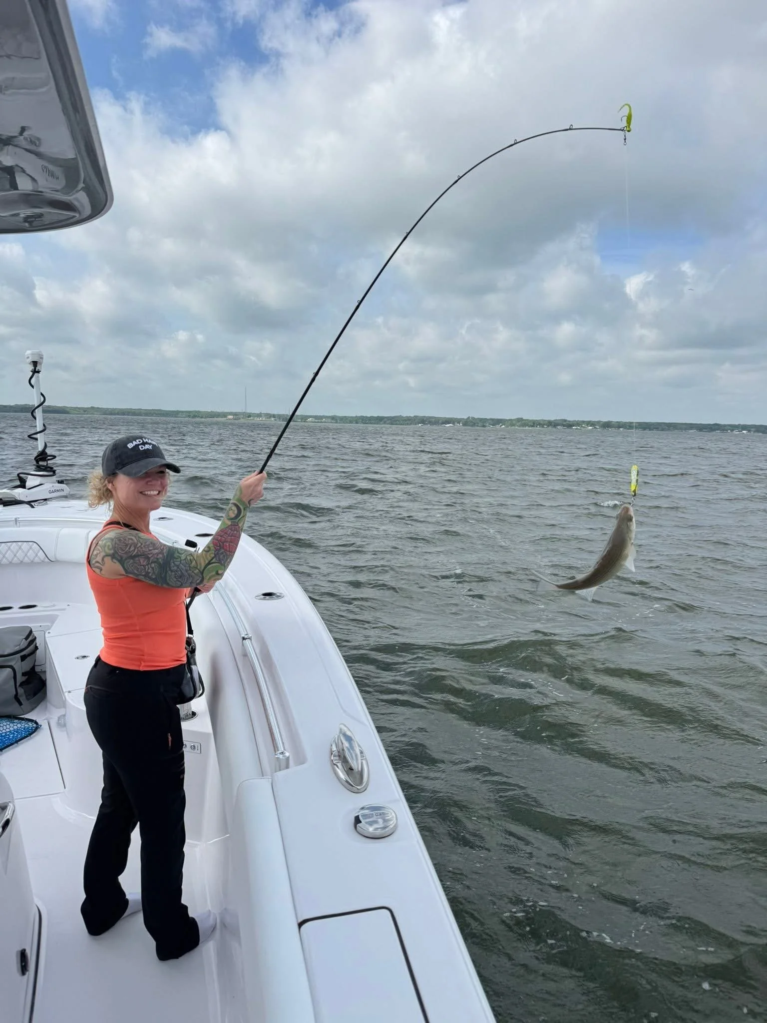 Woman on boat fishing, holding a fishing rod with a fish caught, over water with cloudy sky.