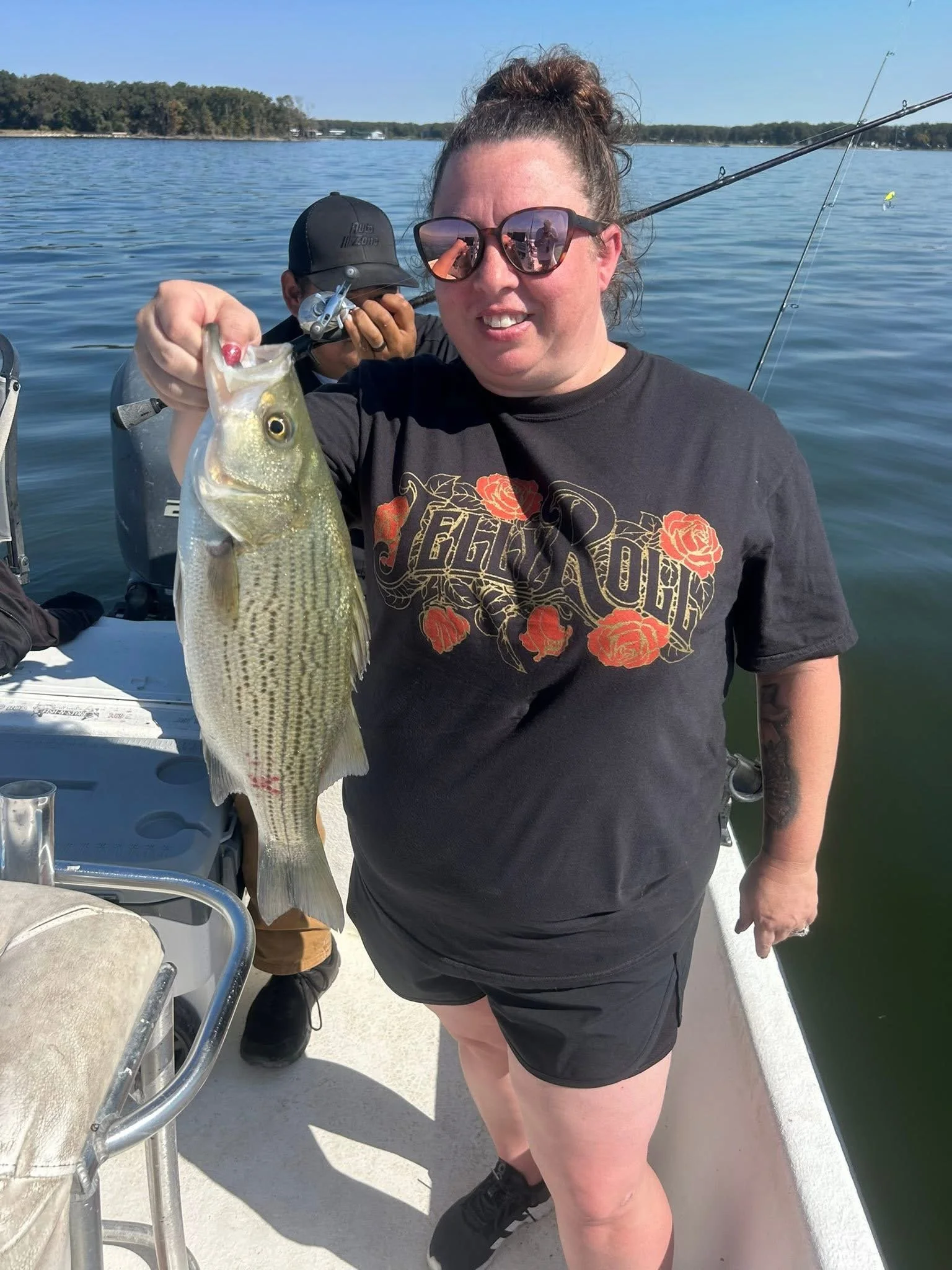 Woman holding a large fish on a boat with water and trees in the background.