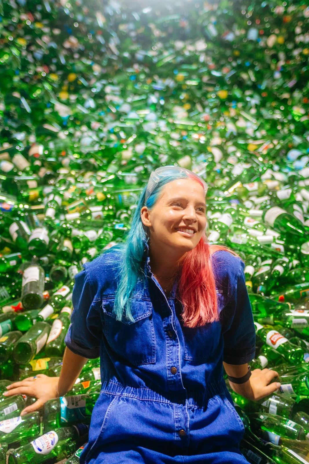 Franziska Trautmann aka "glass girl" and keynote speaker sitting among a large pile of green glass bottles, smiling at the camera. Book glass girl Franziska Trautmann to speak at your event or conference or college campus