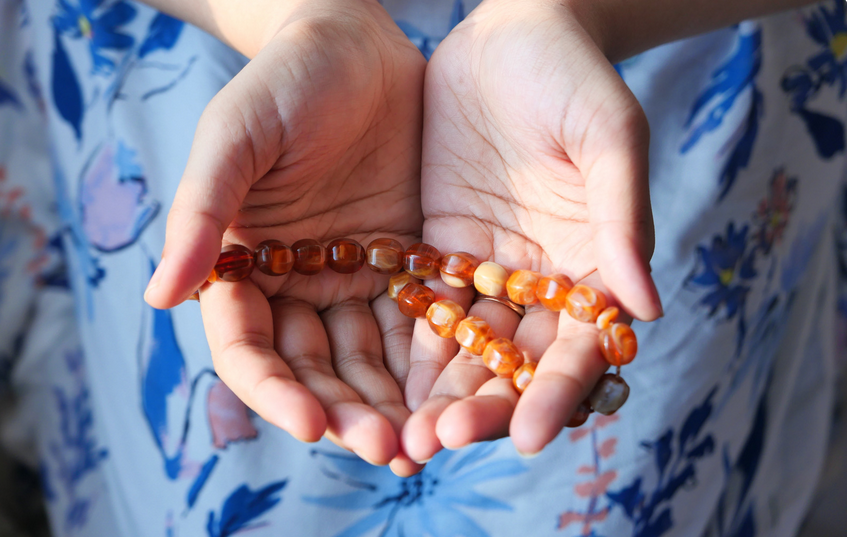 Someone holding an amber-colored beaded necklace or bracelet in their hands.