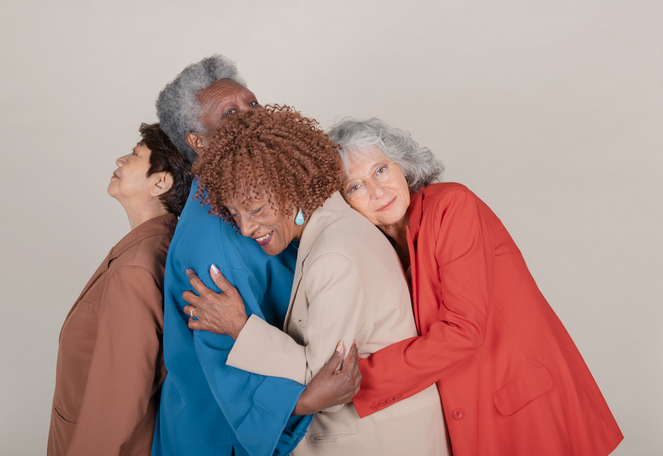 Four women from different generations hugging and smiling together in front of a neutral background.