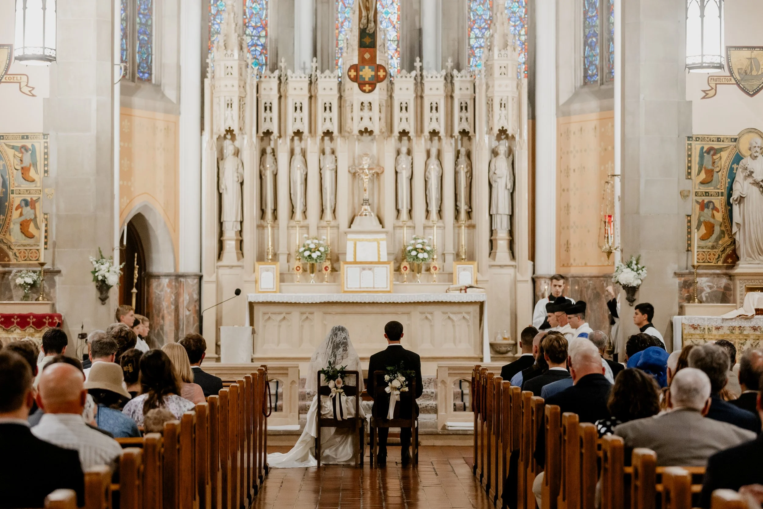 A bride and groom are captured within the context of their wedding day in a Gothic church with white flowers.