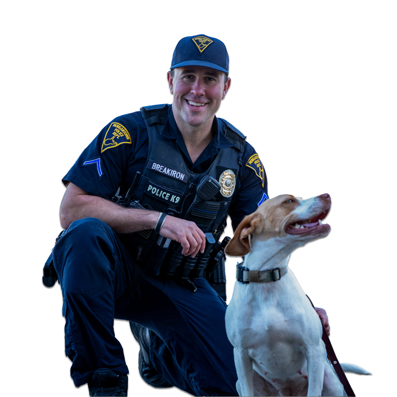 A smiling police officer in uniform kneeling next to a dog, both looking to the right. - Zane Breakiron Uniontown Pa