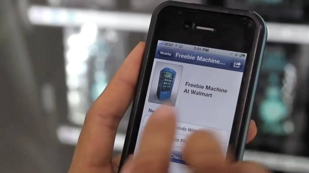 Person using a smartphone displaying a Facebook post titled 'Freebie Machine At Walmart' with an image of a blue vending machine.
