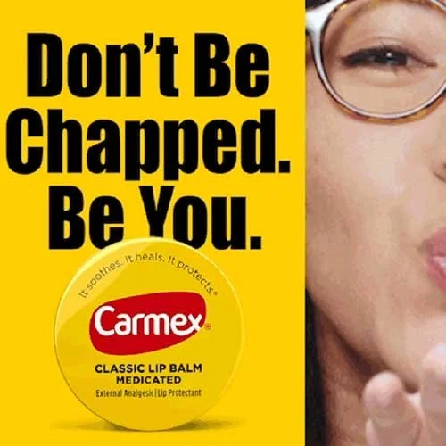 Advertisement for Carmex lip balm with the slogan "Don't Be Chapped. Be You." and a partial image of a woman applying lip balm.