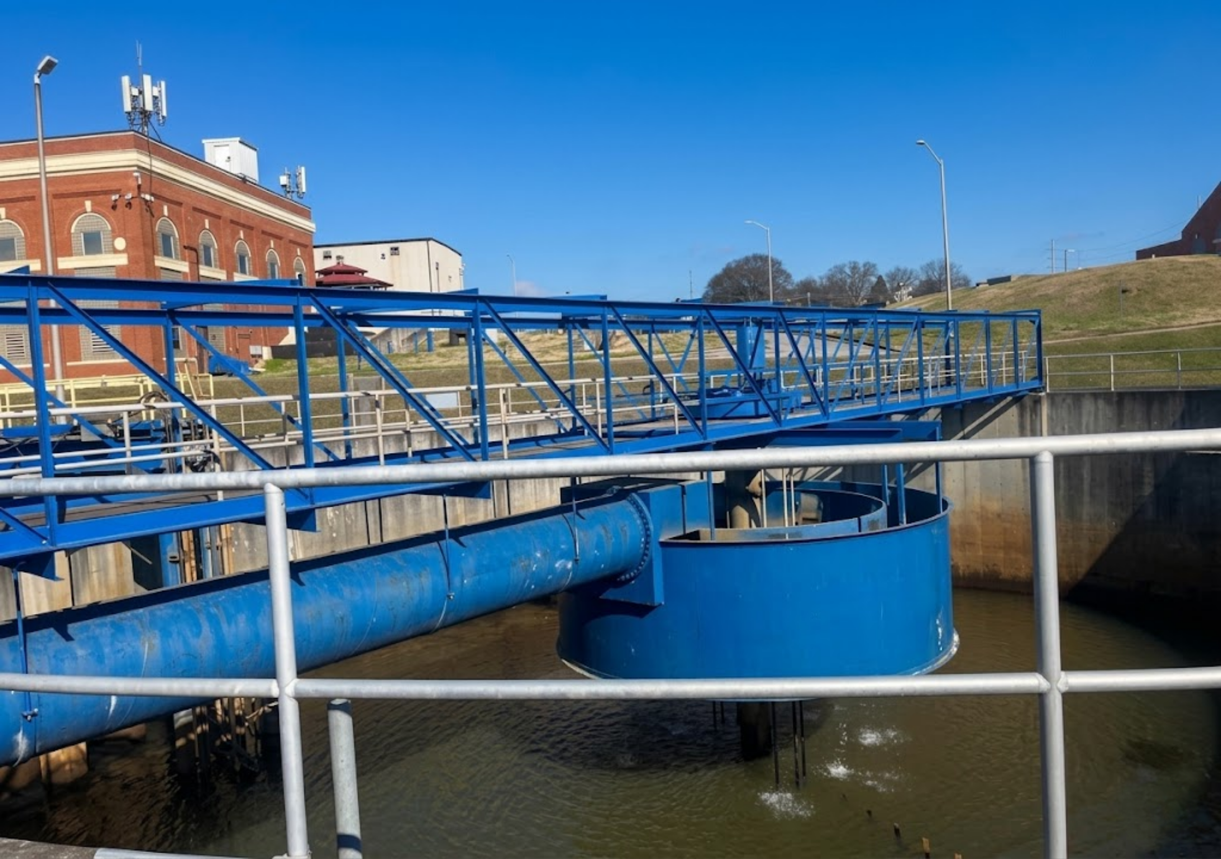 Blue water slide structure over a river with a brick building and blue sky in the background.