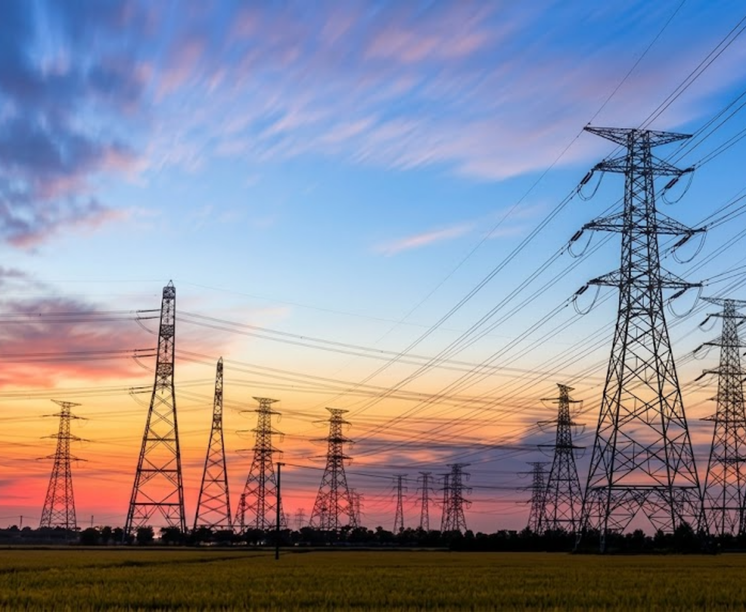 Multiple electrical transmission towers at sunset against a colorful sky with clouds.
