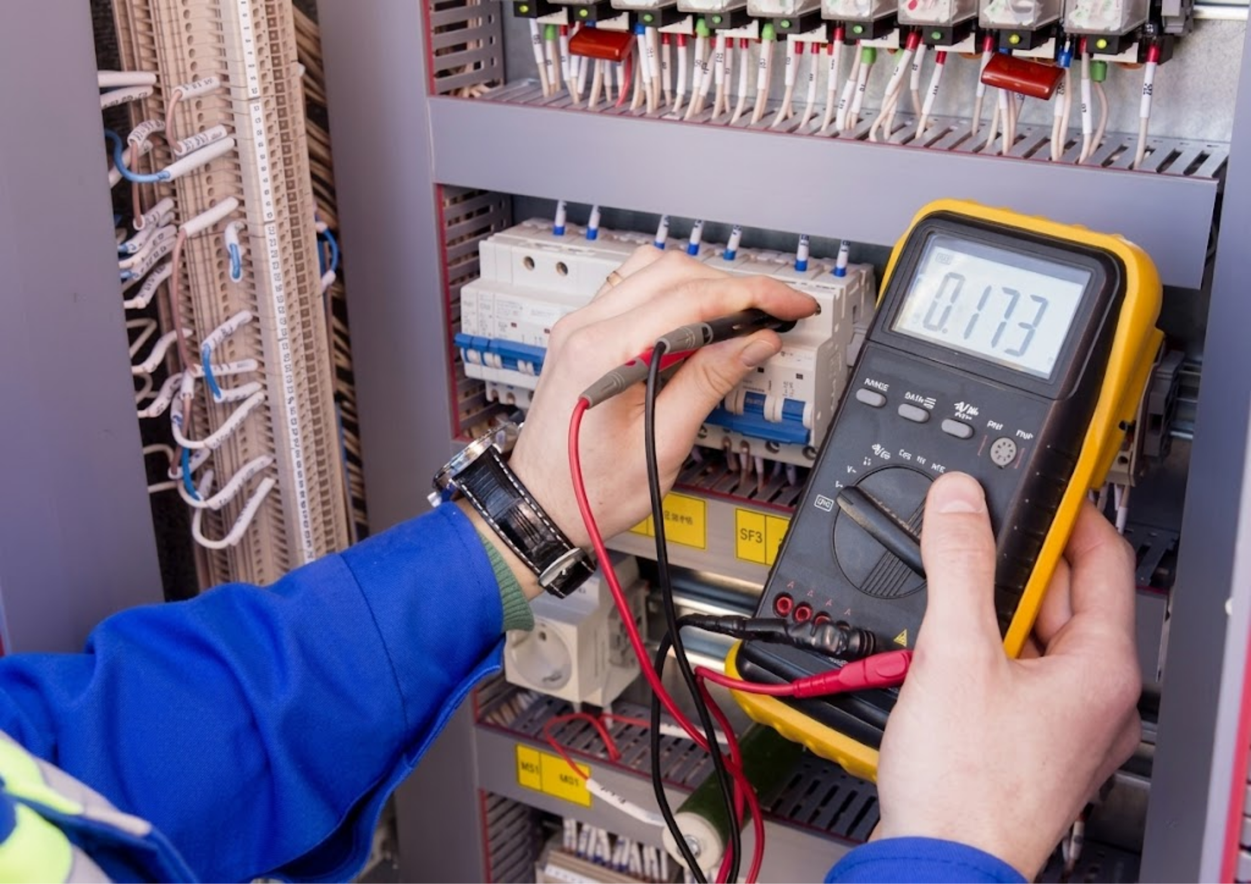 A person testing or measuring electrical circuits inside a control panel using a multimeter.