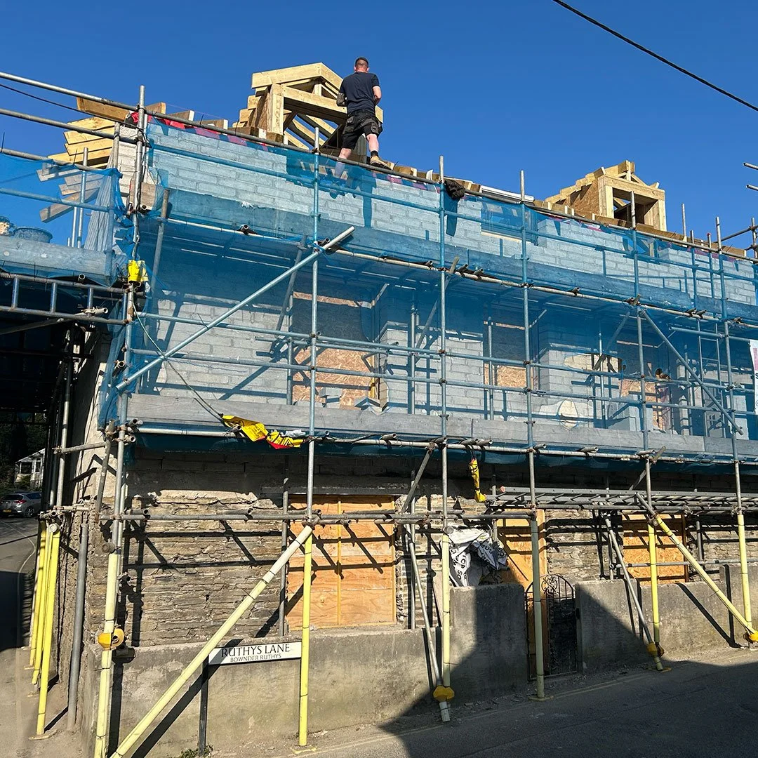 Undergoing construction of a building with scaffolding, blue safety netting, and new wooden framing on top, against a clear blue sky.
