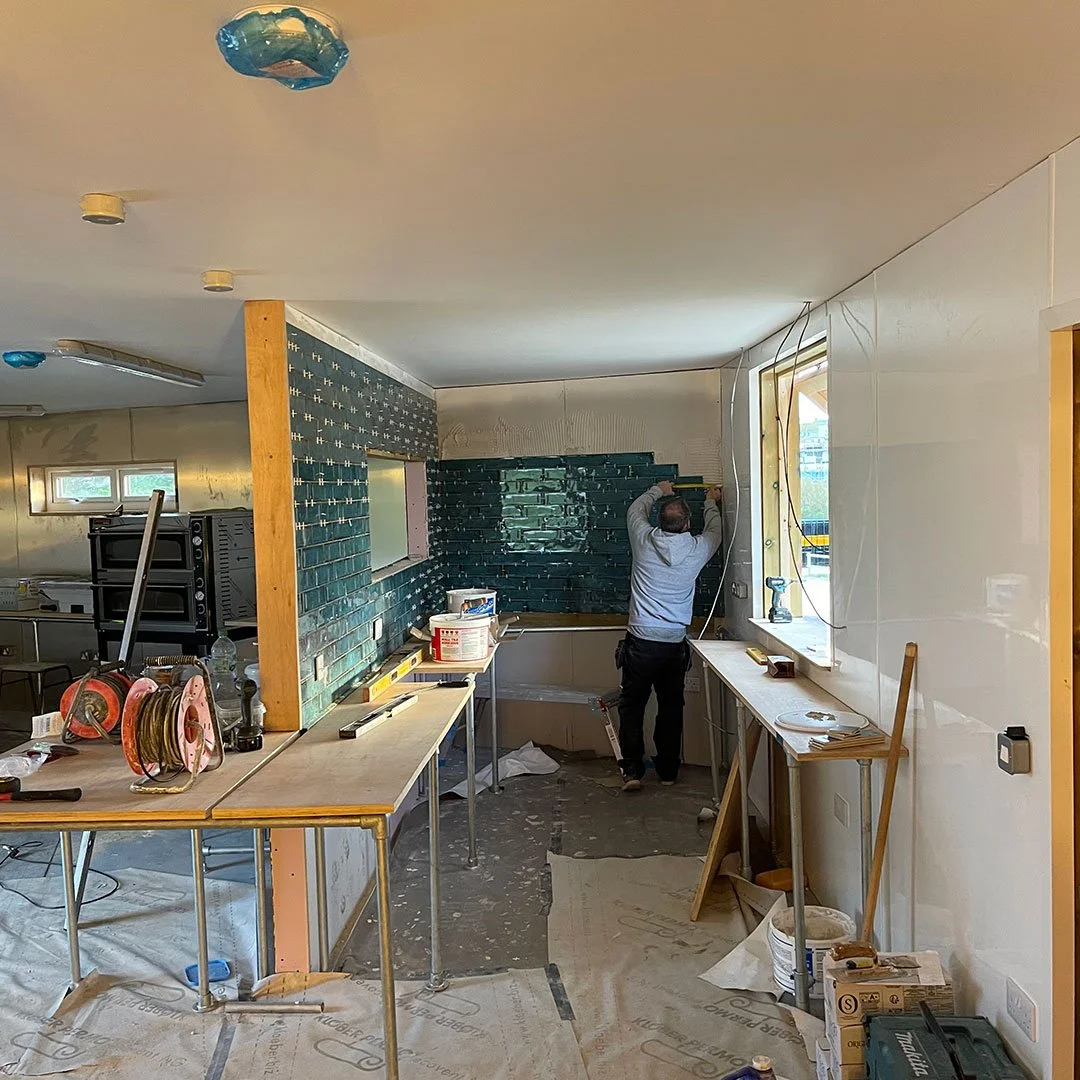 A worker installing green subway tiles in a kitchen under renovation.