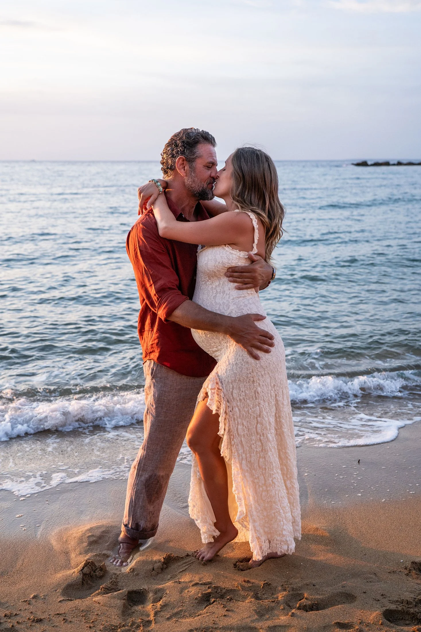 Engaged couple kissing by the sea during a golden hour maternity and proposal photoshoot in Italy.