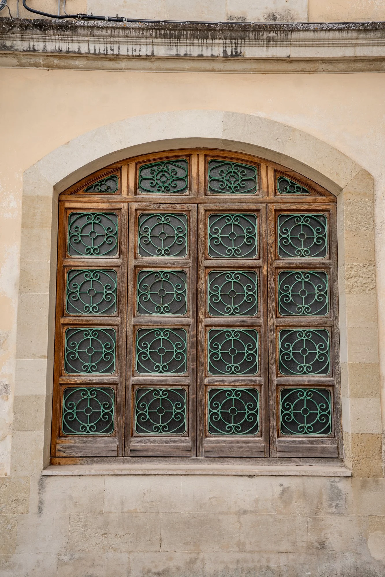  Elegant arched wooden window in a historic stone facade in Otranto's center, captured by a luxury couple photographer in South Italy. 