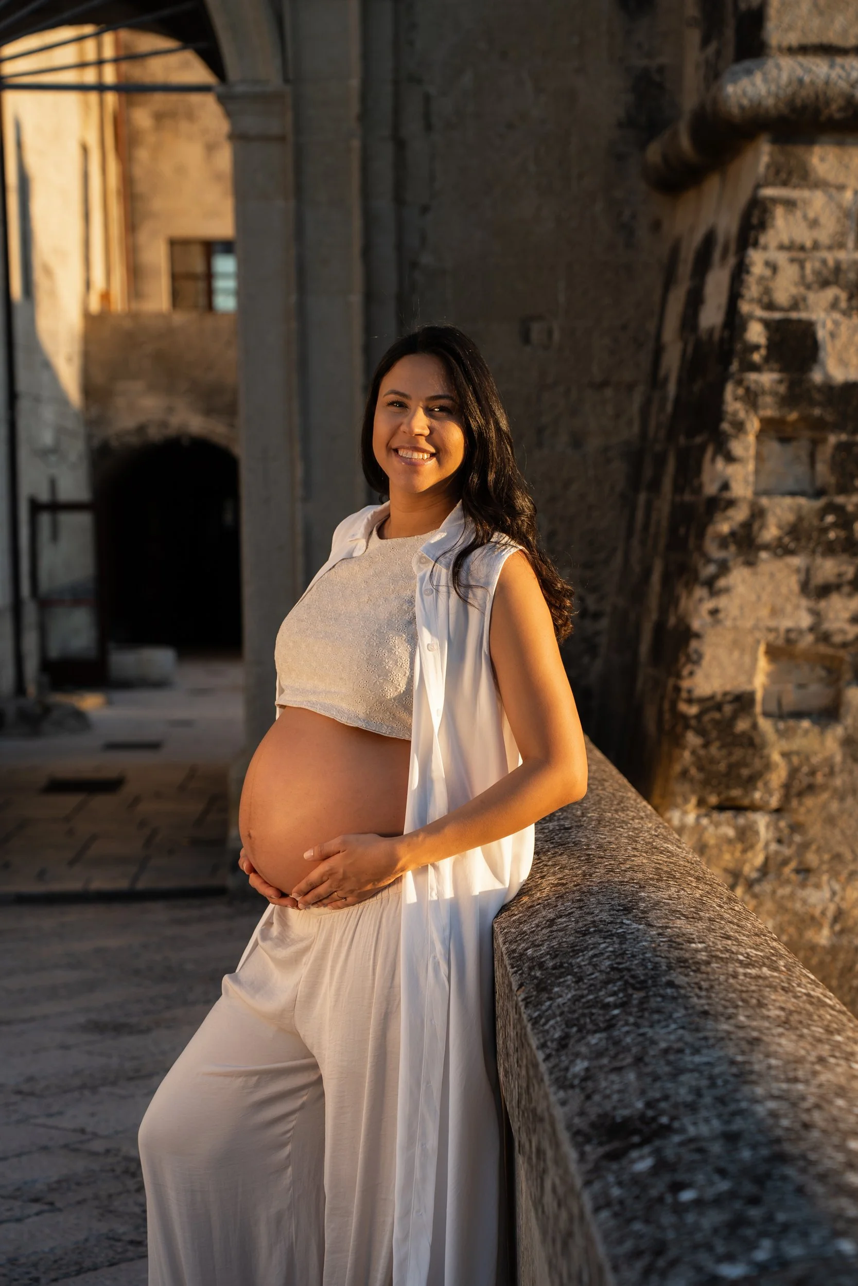 An expecting mother glowing in a beautifully draped white outfit during her fine-art maternity photography session in Lecce, Puglia.