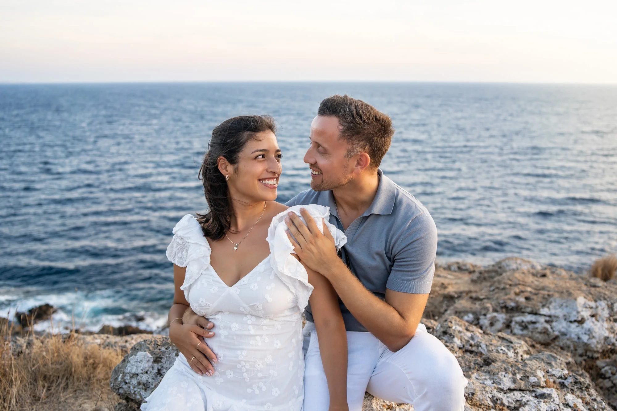 Happy couple celebrating their 5th wedding anniversary laughing by the sea coast in Puglia, Italy.