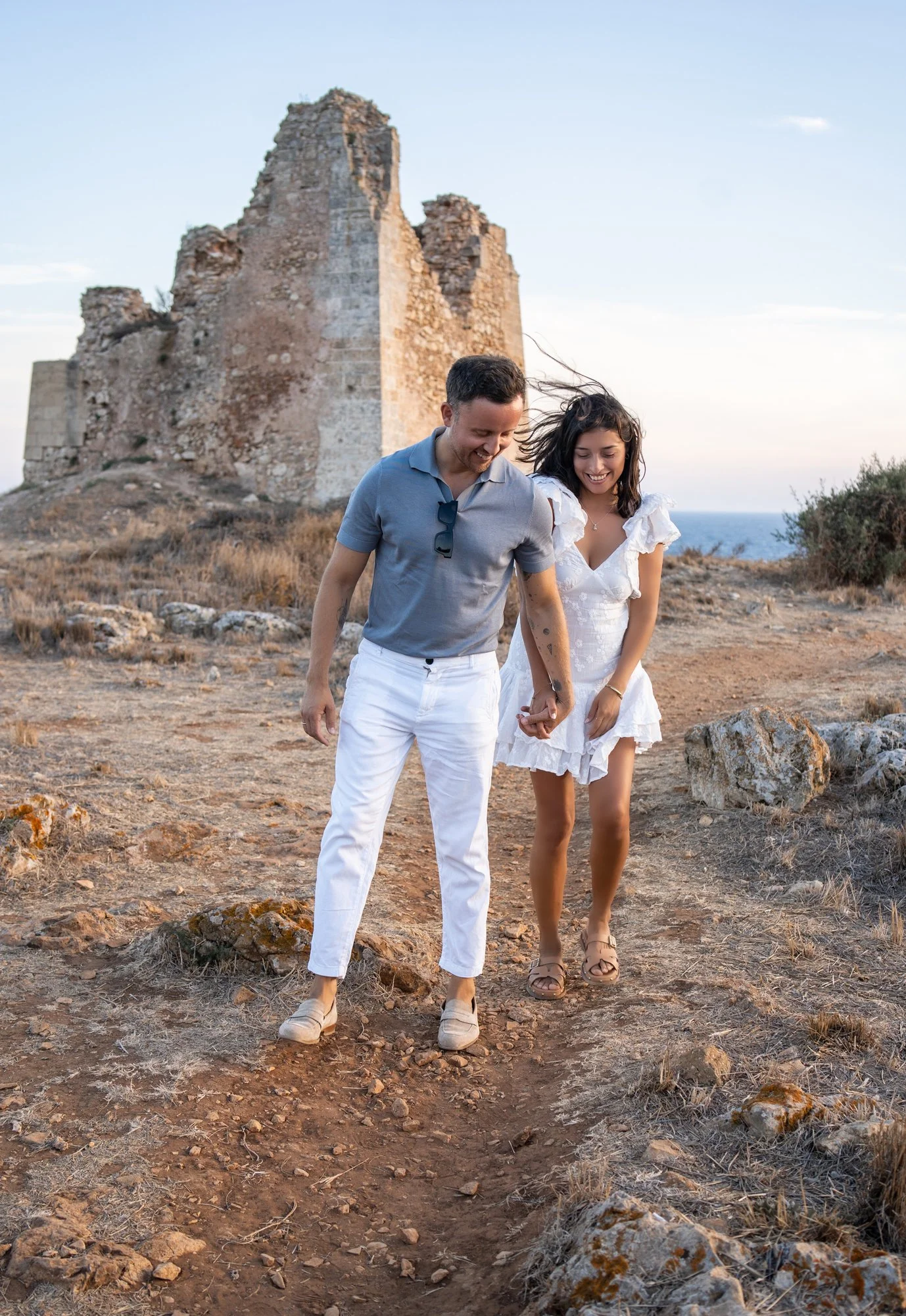 Puglia couple's photographer capturing a beautiful 5th wedding anniversary walk by an ancient stone tower in Southern Italy.