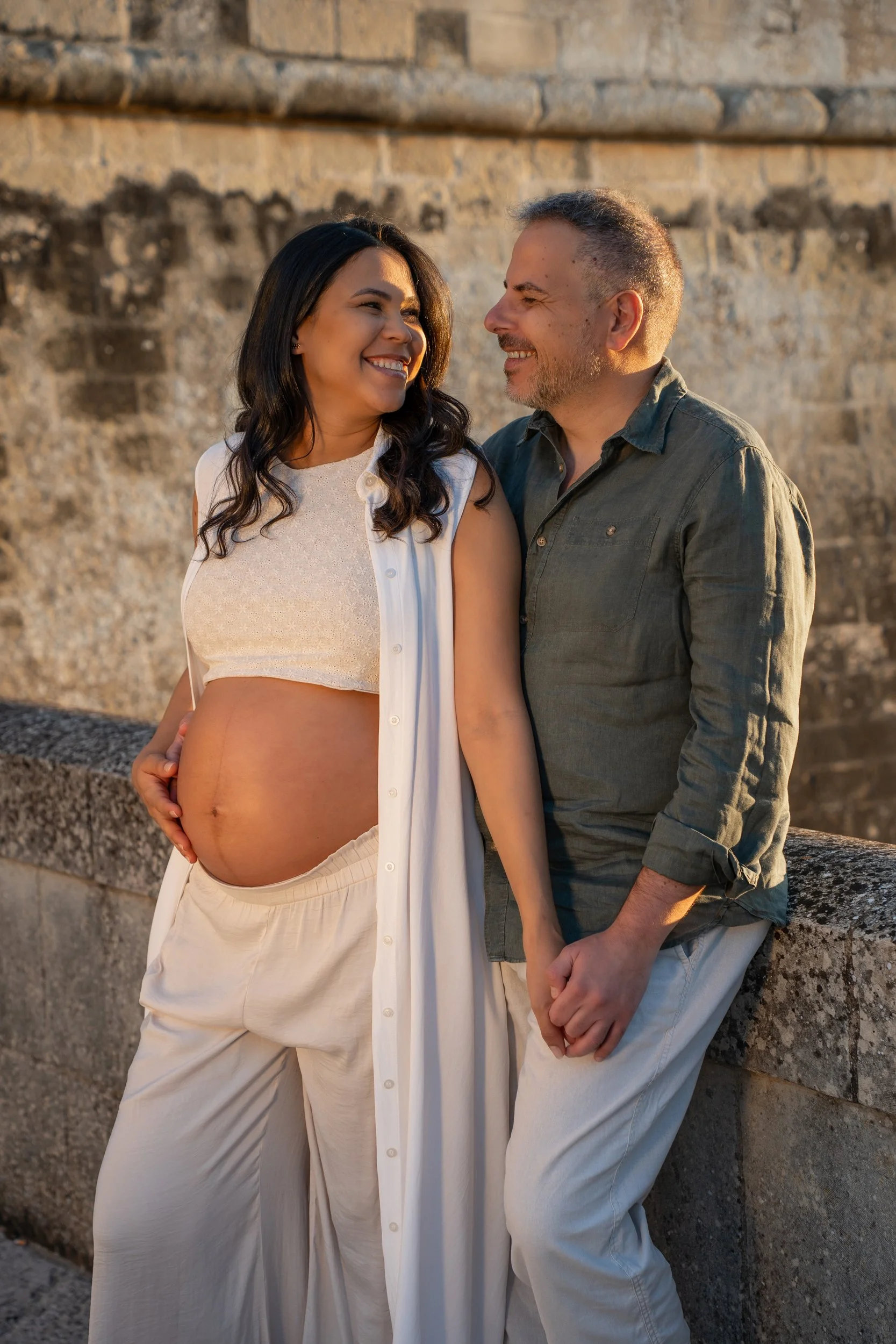 Expecting parents standing by the historic stone walls of Acaya Castle, enjoying a relaxed and romantic maternity session near Lecce, Southern Italy