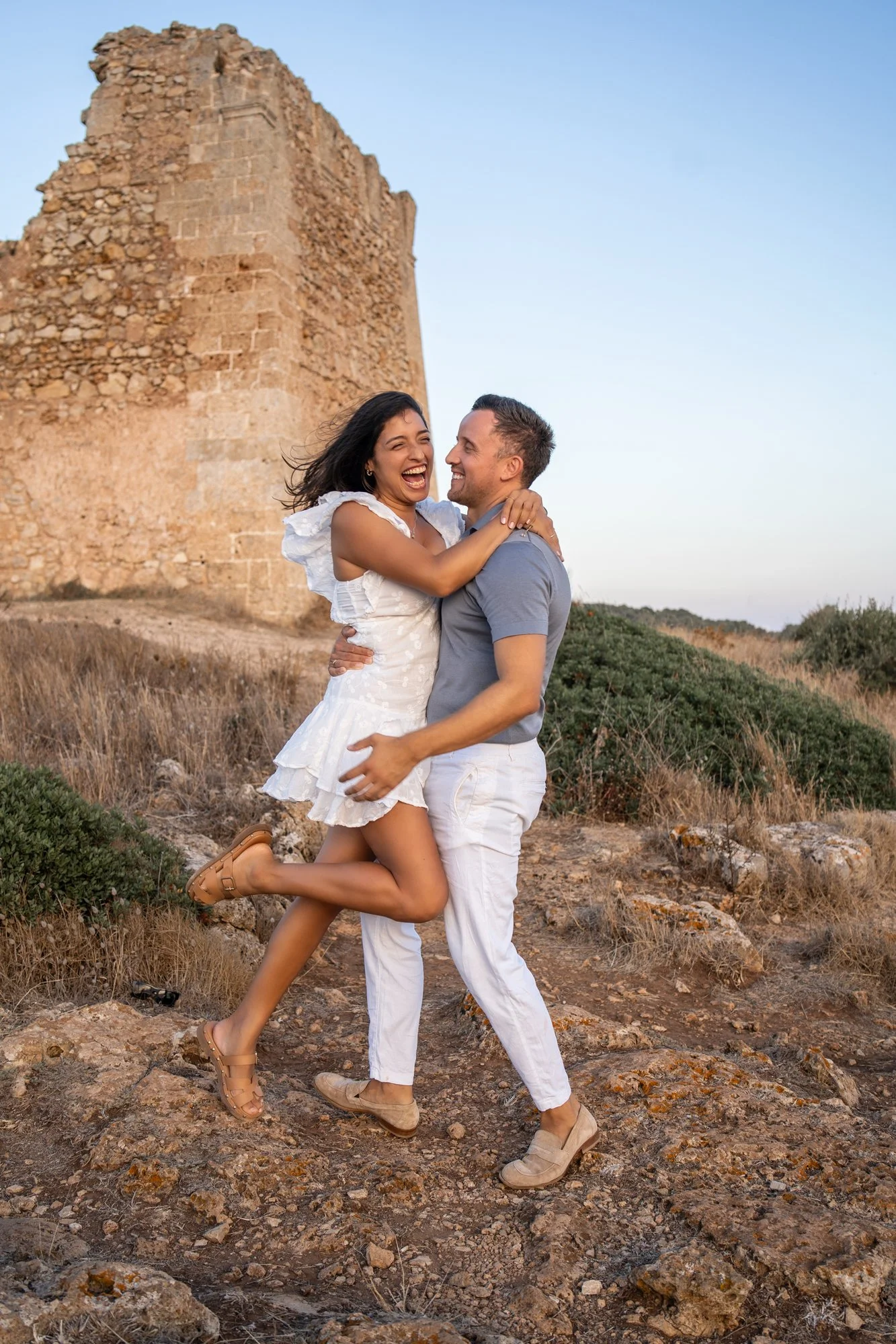 Happy couple celebrating their 5th wedding anniversary laughing by the sea coast in Puglia, Italy.
