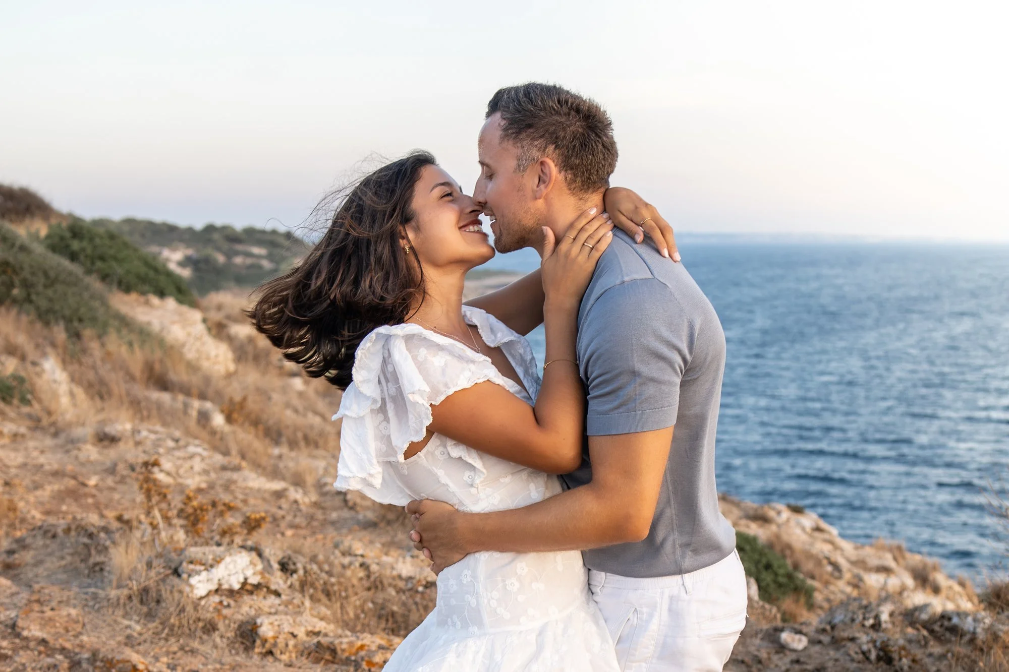 Romantic couple walking near a historic coastal tower during a golden hour photoshoot in Puglia, Italy.