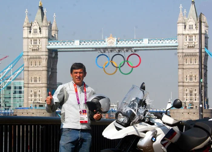 Persona en Londres con Torre de Londres de fondo y los aros olímpicos, junto a una motocicleta BMW, dando pulgar arriba.