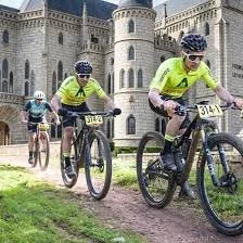 Cuatro ciclistas participando en una carrera en un parque con un castillo en el fondo, todos con cascos y ropa deportiva