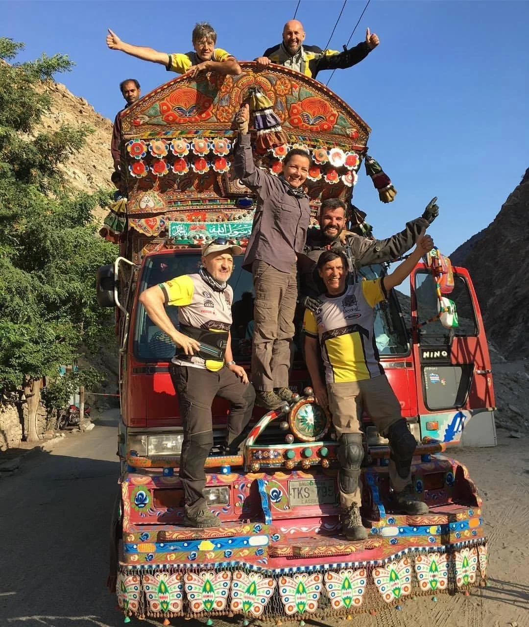 Grupo de personas en un camión decorado con detalles coloridos y patrones tradicionales, disfrutando en un entorno montañoso con cielo claro.
