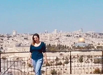 Woman walking on a balcony overlooking Jerusalem with the Dome of the Rock in the background.