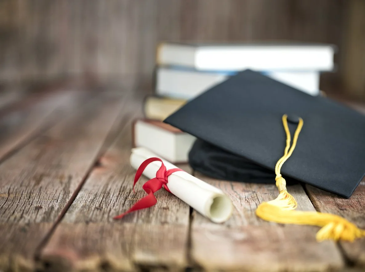 Graduation cap, diploma, and books on a wooden surface.