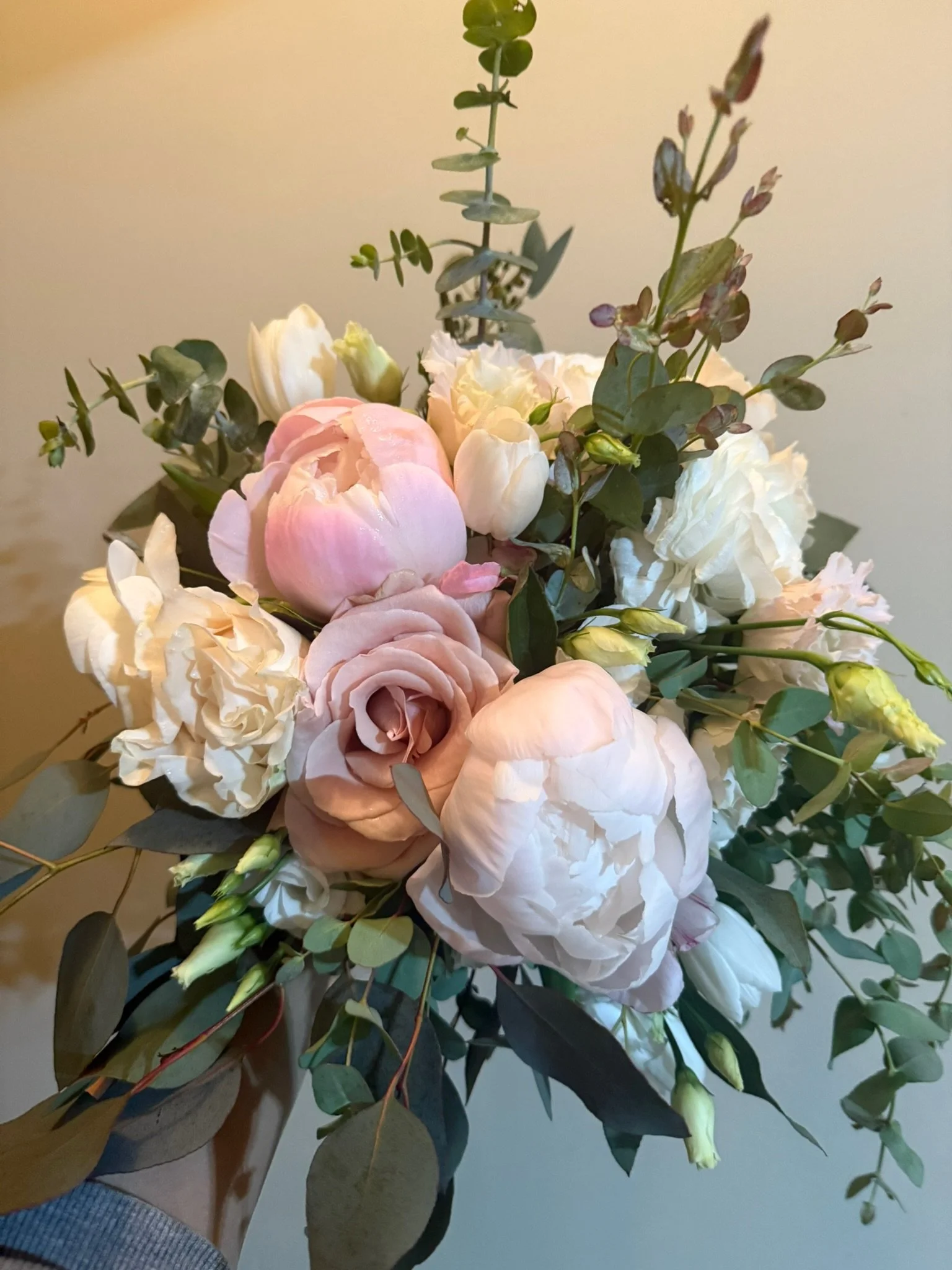 A bouquet of flowers including white roses, pink peonies, and eucalyptus leaves.