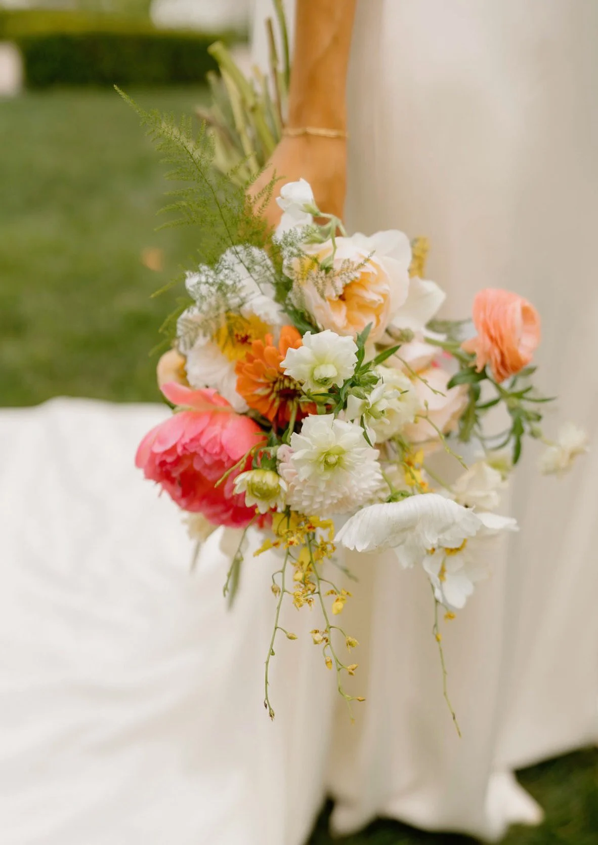 Close-up of a colorful flower arrangement with white, peach, pink, and orange flowers, and greenery, attached to a wooden surface indoors.