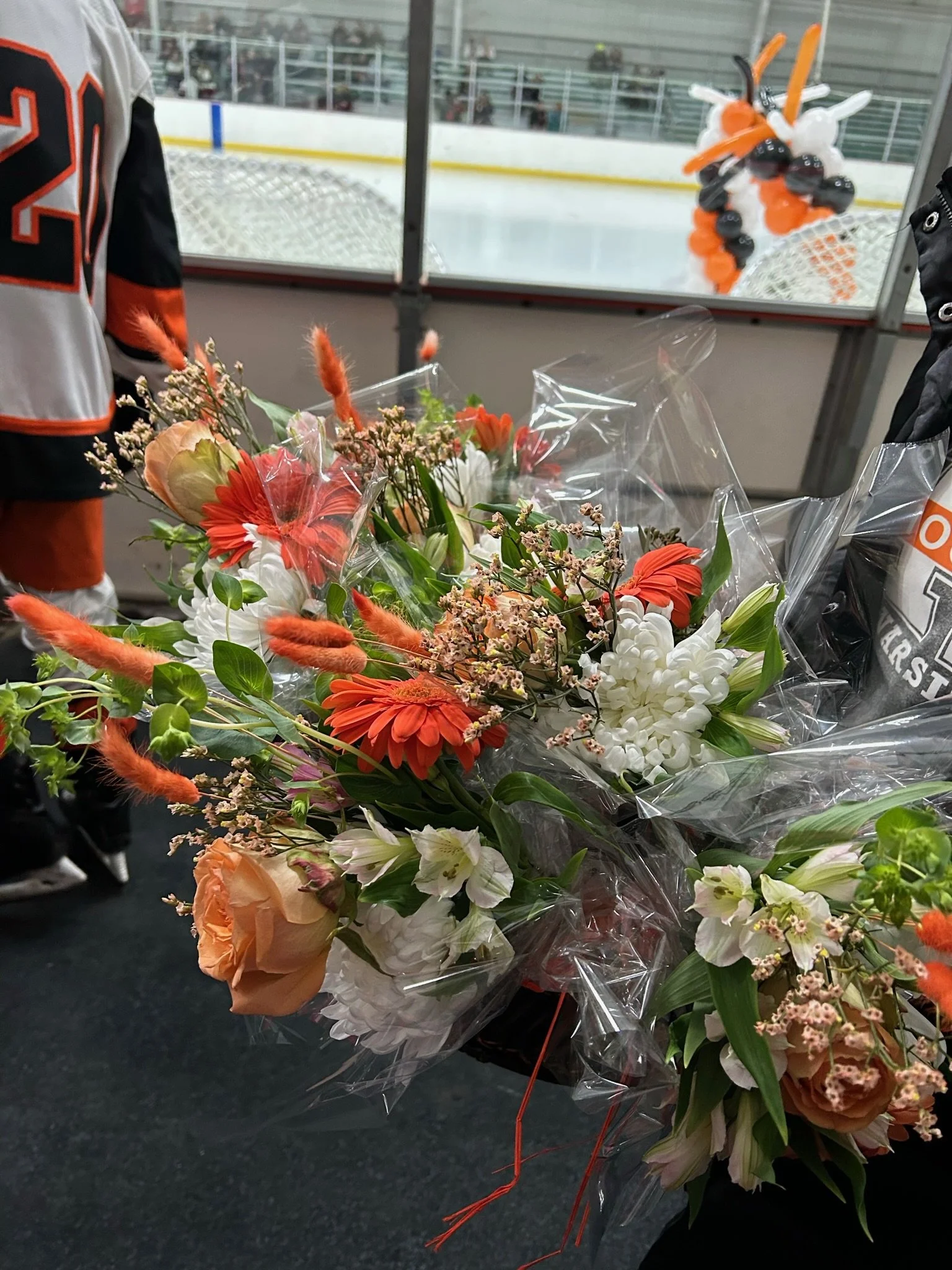 Bouquet of mixed flowers wrapped in plastic on a surface, set against the background of an ice hockey rink.