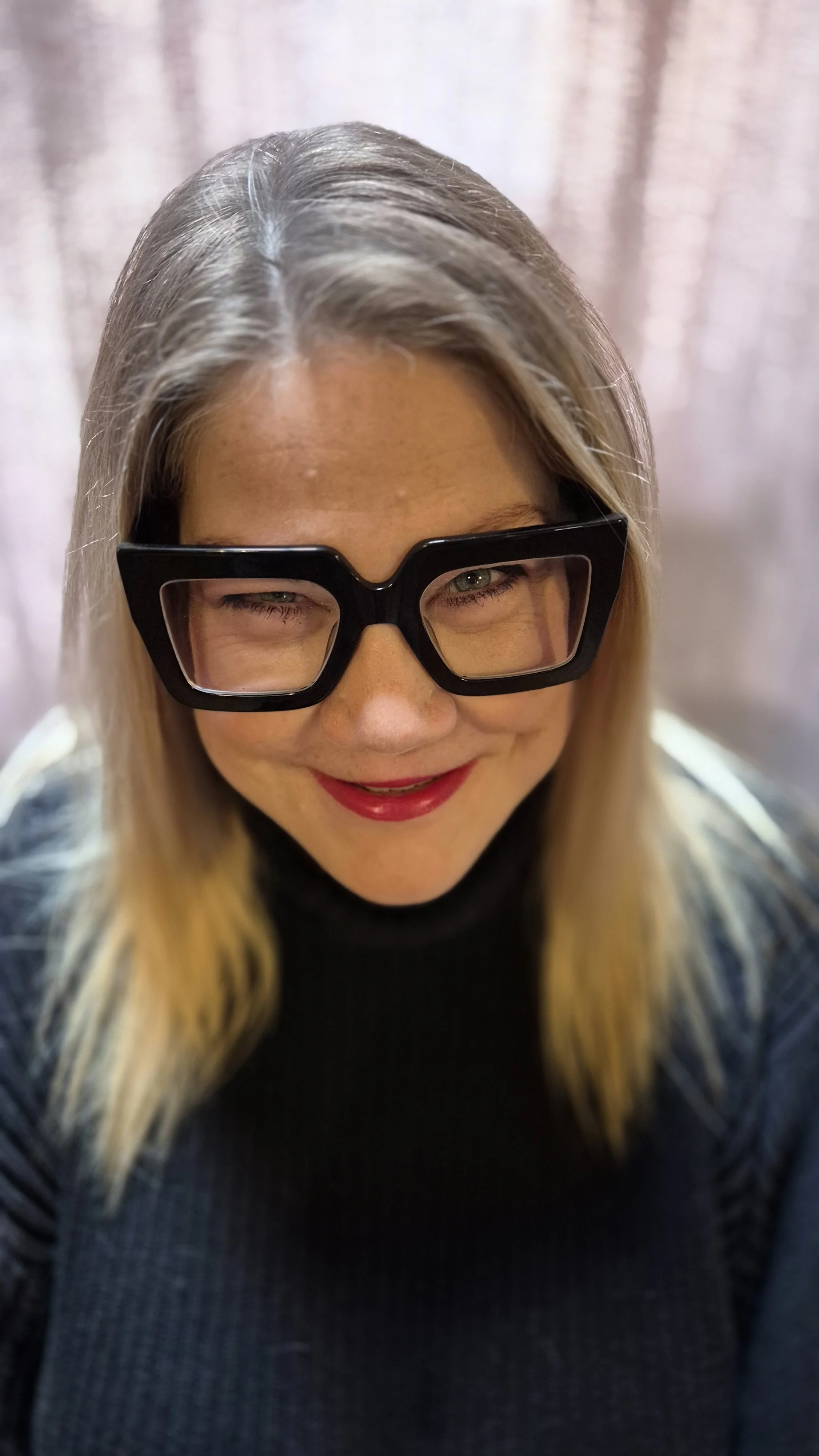 A picture of Susie smiling in funky thick framed black glasses