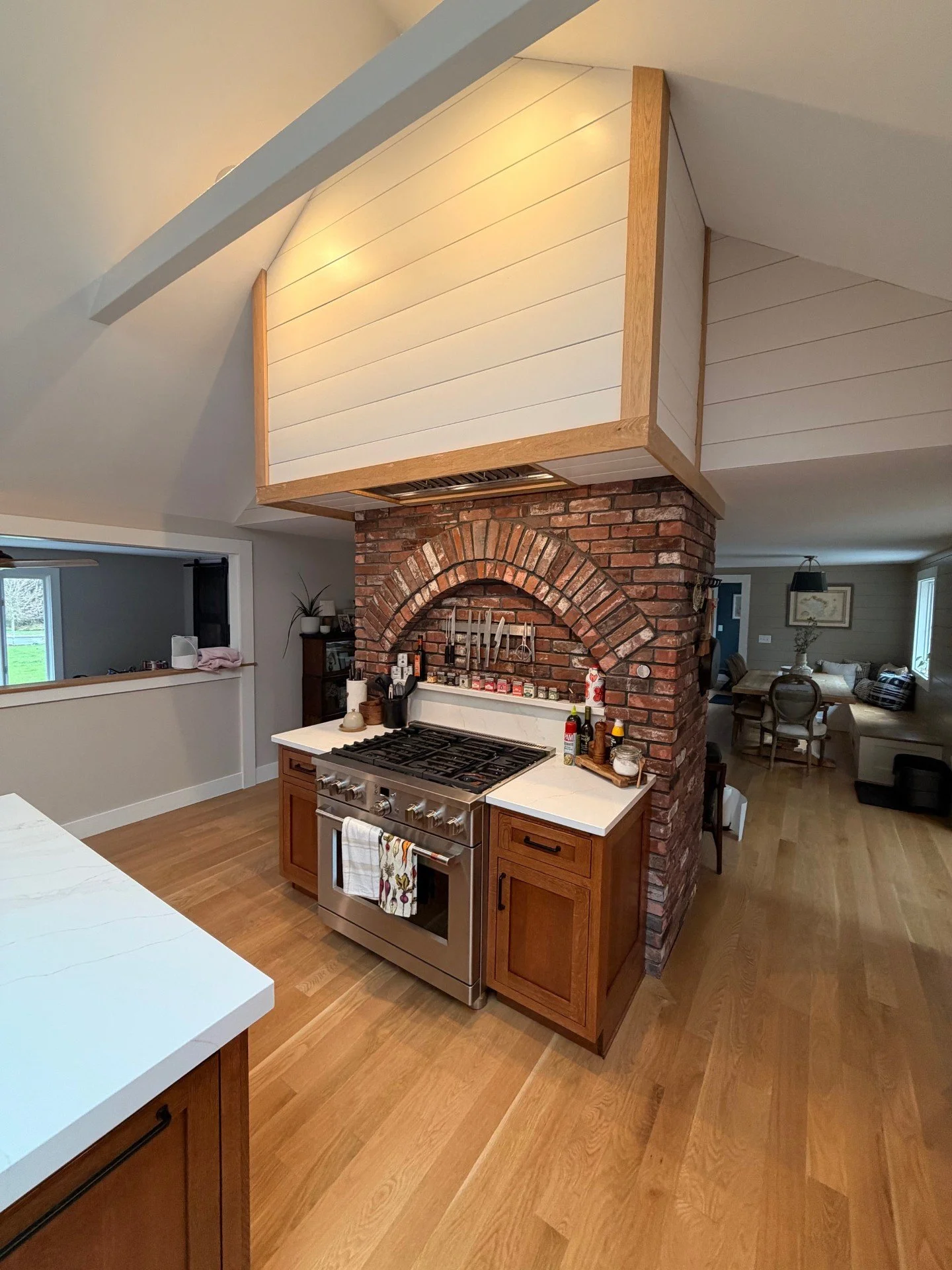 Kitchen with brick archway and stove, wooden cabinets, white countertops, and wooden flooring.