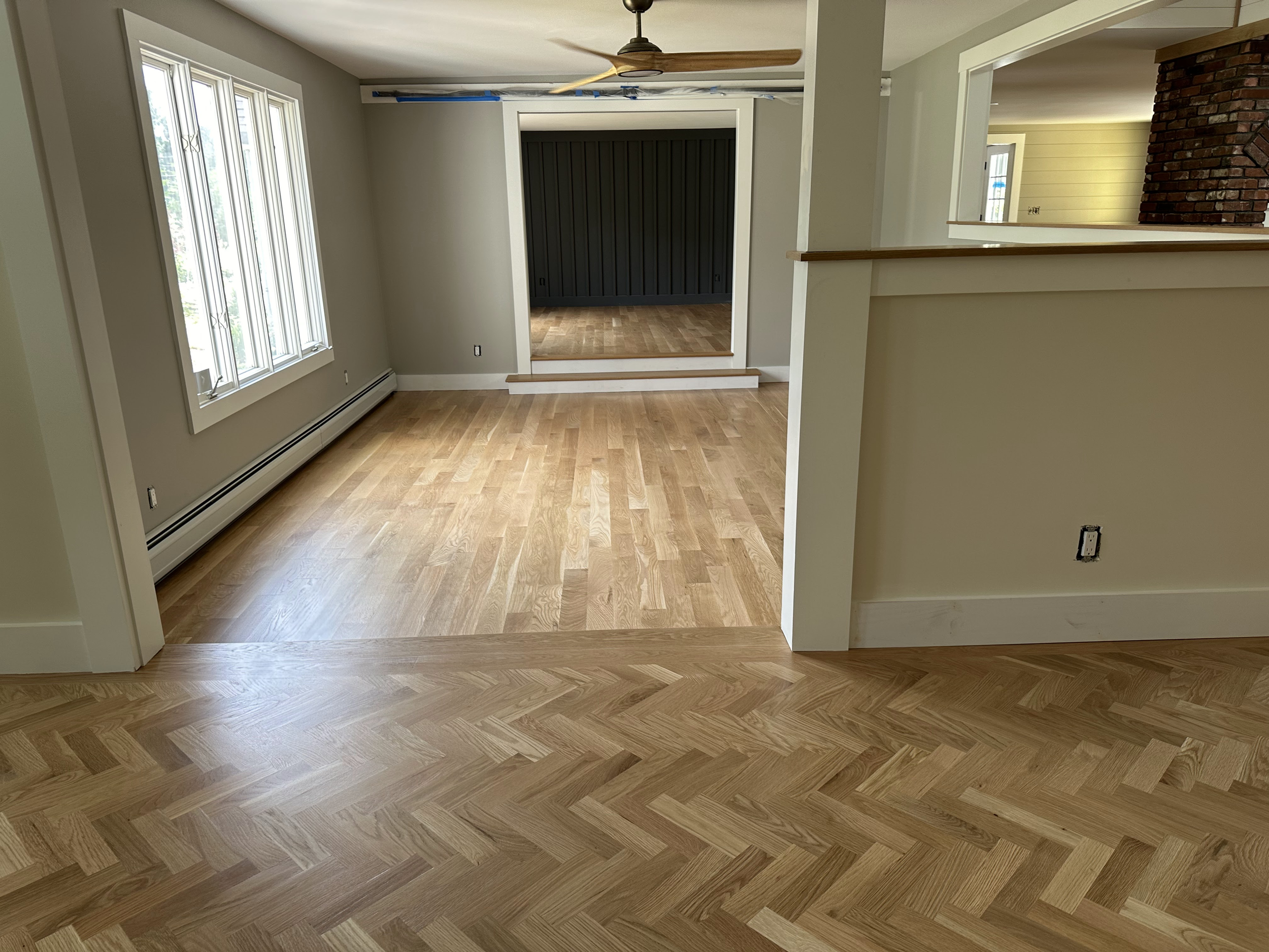 Empty room with wood flooring, a window with white trim, a black sliding door, and a partial brick fireplace wall.