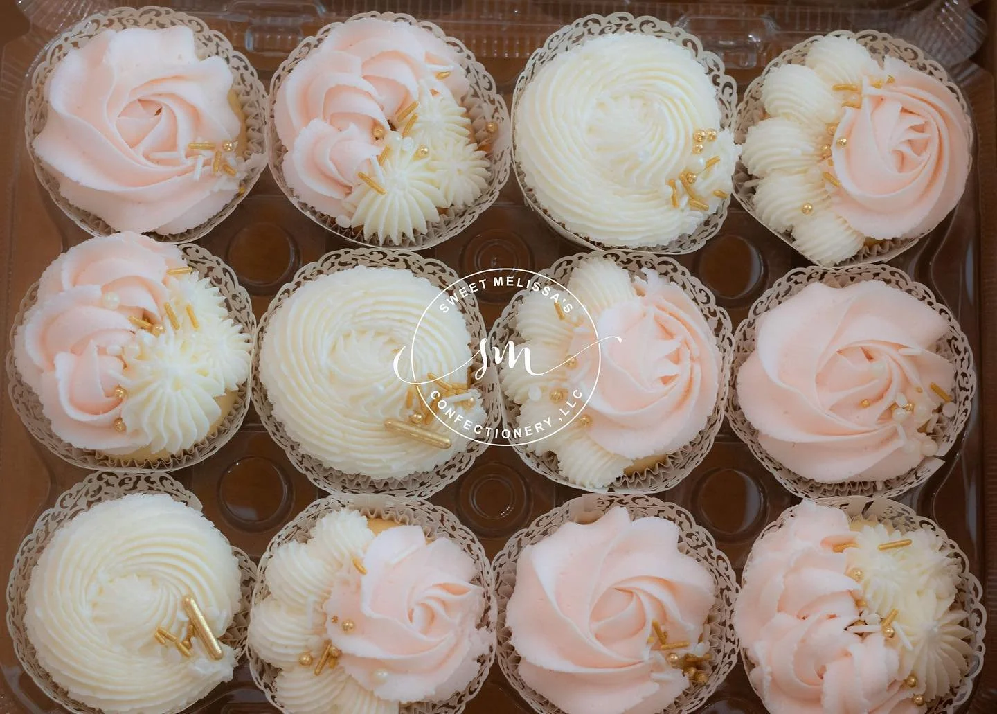 Box of 12 decorated cupcakes with pink and white swirls, pearl and gold accents.