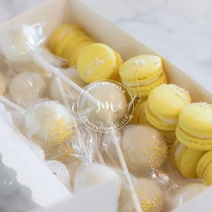Yellow macarons and white decorated cake pops inside a box