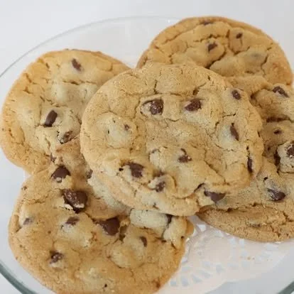Four chocolate chip cookies on a clear glass plate.