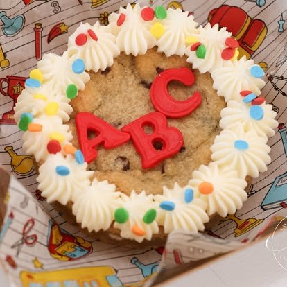 Heart-shaped cookie decorated with white frosting, colorful sprinkles, and red letters 'A B' and a red letter 'C' on top.