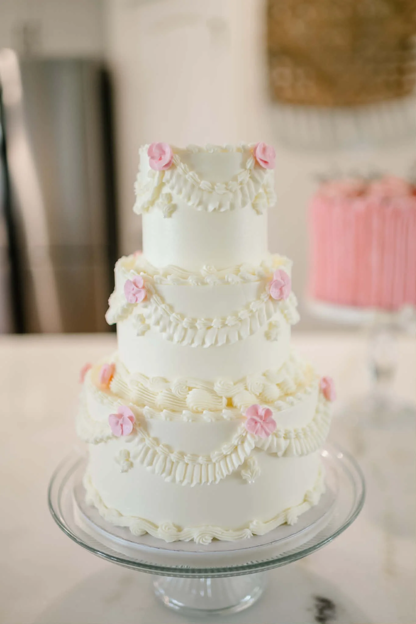 A three-tiered white wedding cake decorated with pink and white flowers, displayed on a glass stand.
