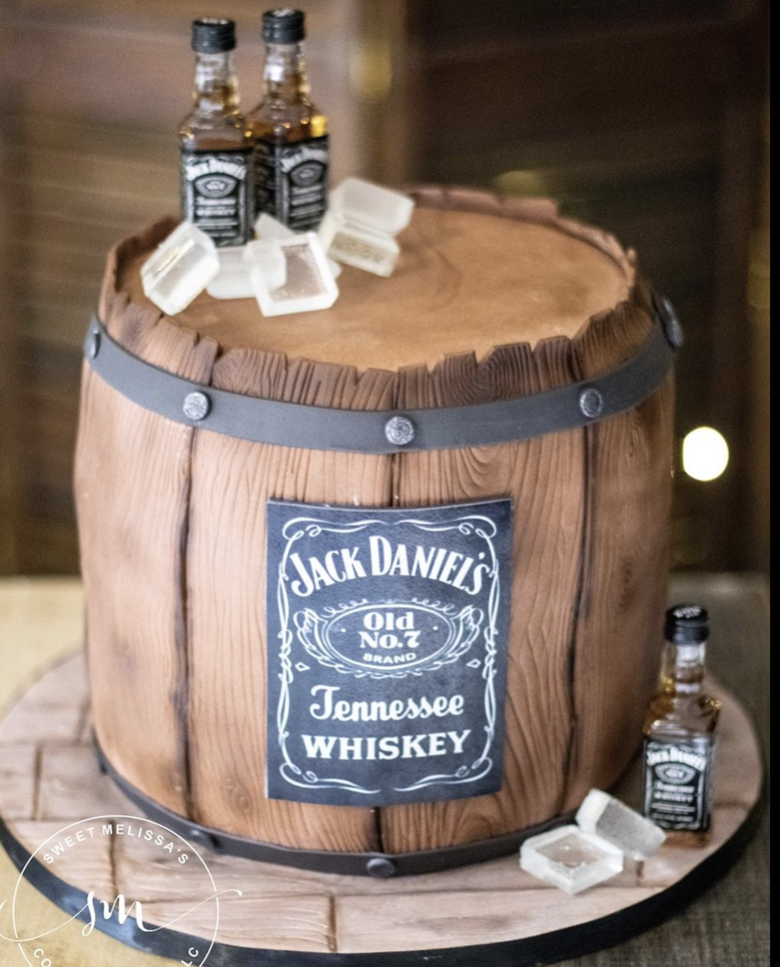 A wooden barrel with Jack Daniel's whiskey bottles and ice cubes on top, with more bottles on the side and a Jack Daniel's label on the barrel.