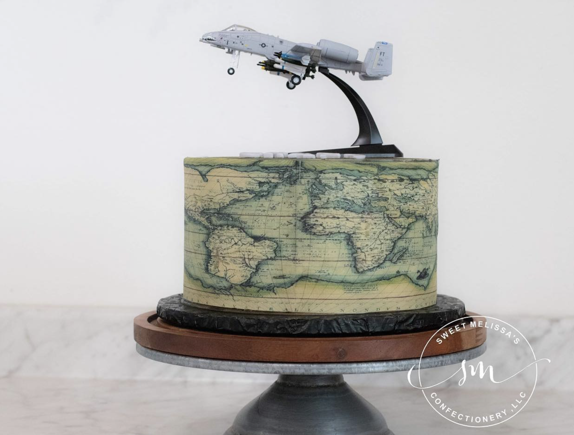A detailed model airplane mounted on a stand featuring a map design, displayed on a two-tiered wooden and metallic base.