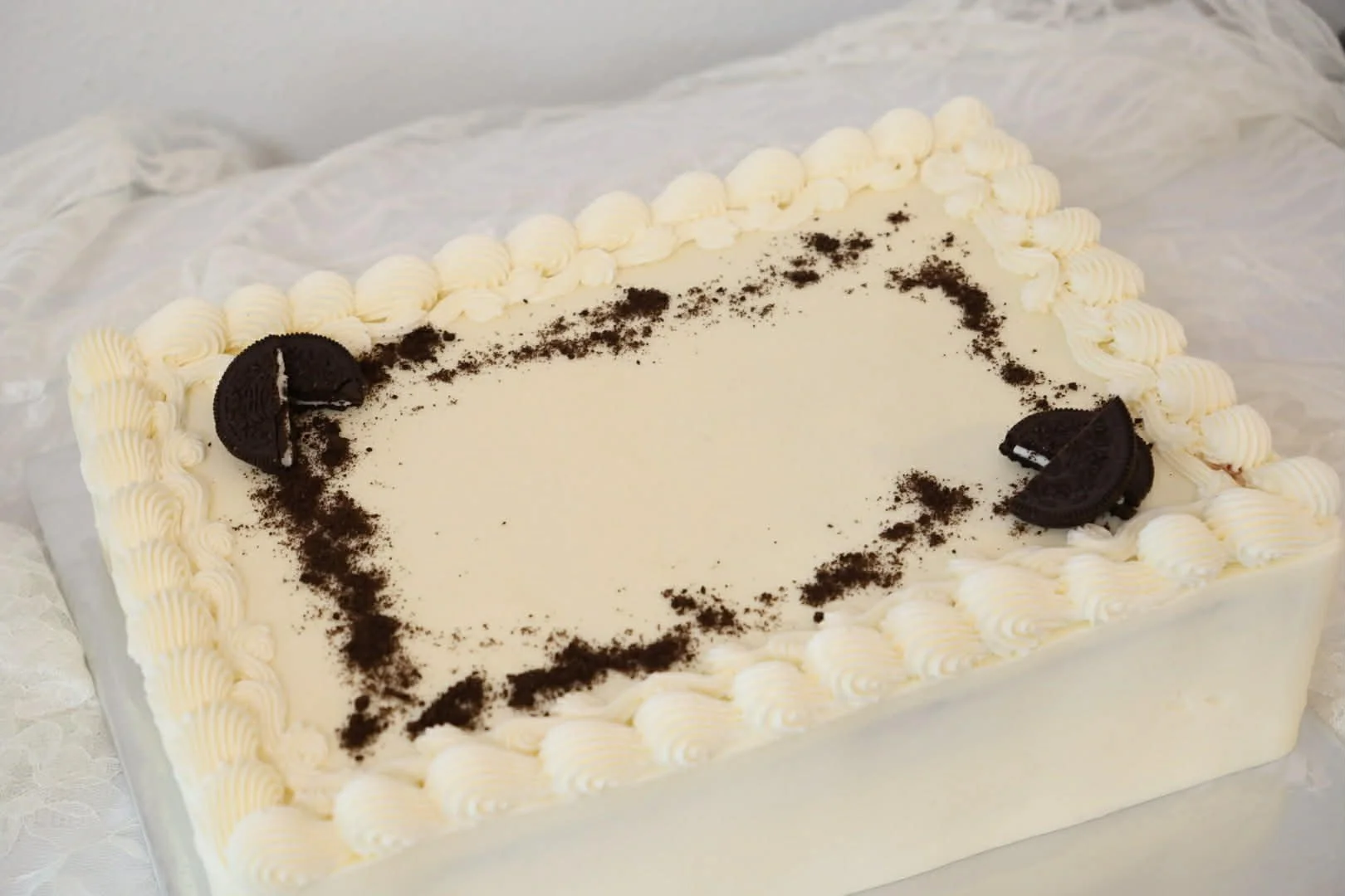 Rectangular cookies and cream cheesecake with Oreo cookies decoration, decorated with whipped cream border and cookie halves on top, surrounded by white paper or cloth.