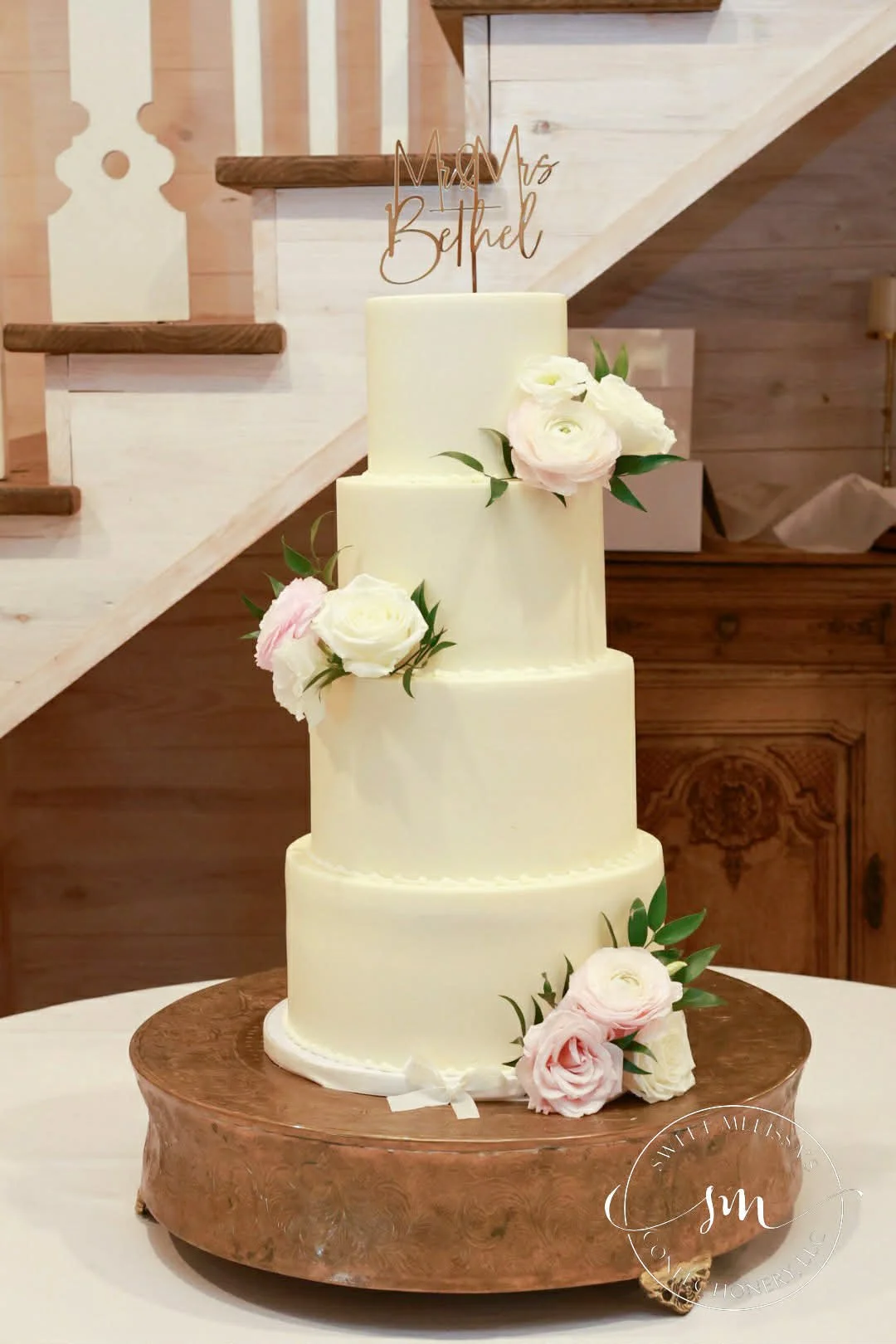 Two-tier white wedding cake with green marble-like streaks, decorated with white roses and green leaves, on a glass cake stand against a neutral background.