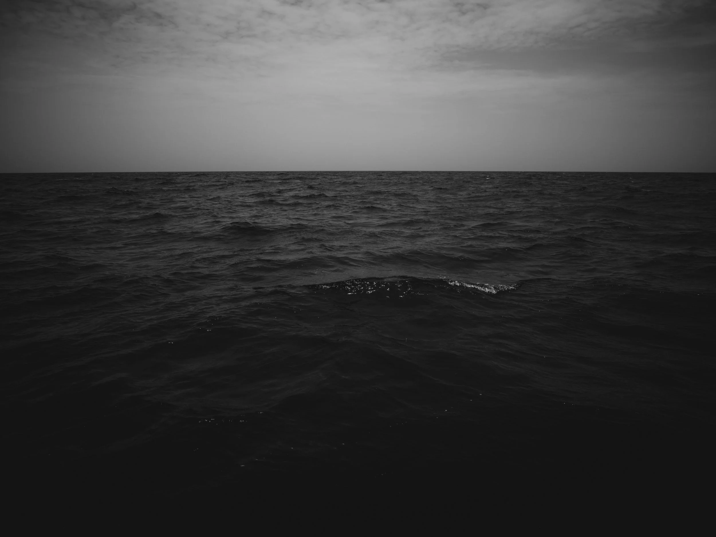 Black and white photo of the ocean with waves and a cloudy sky.