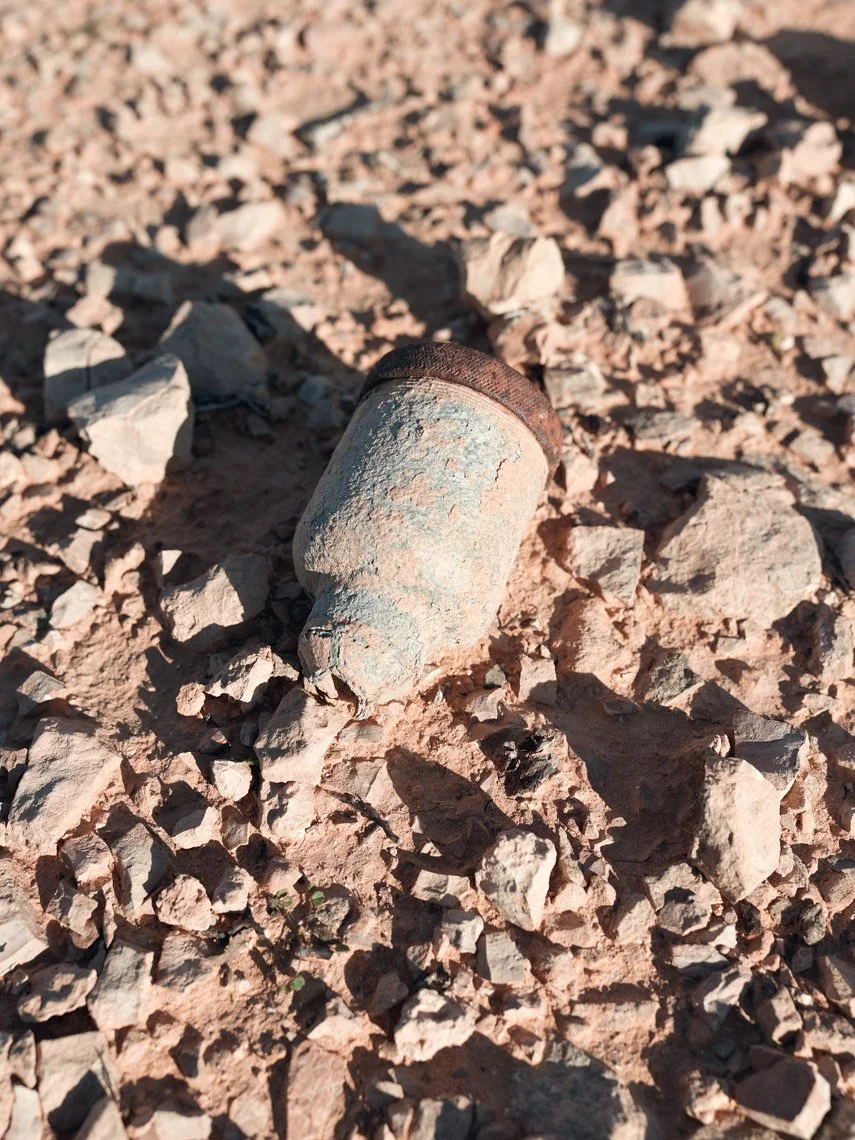 Close-up of a rusted, grenade from World War II lying on rocky, dirt ground.
