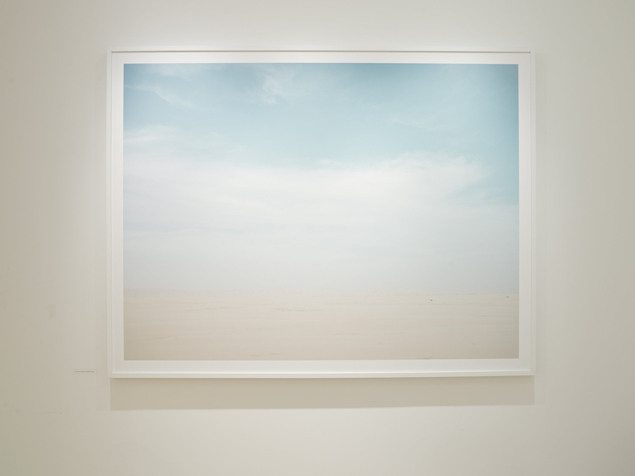 A framed photo of a blue sky with some clouds on a white wall.